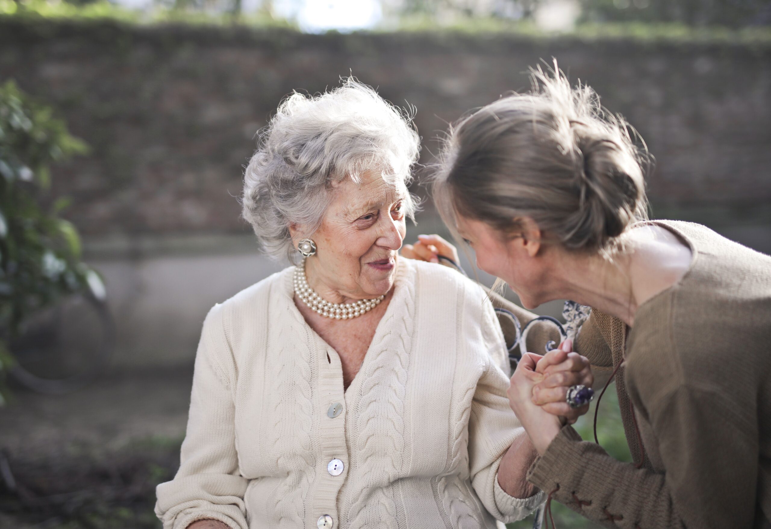 Two older women smiling and enjoying a friendly conversation together outdoors.